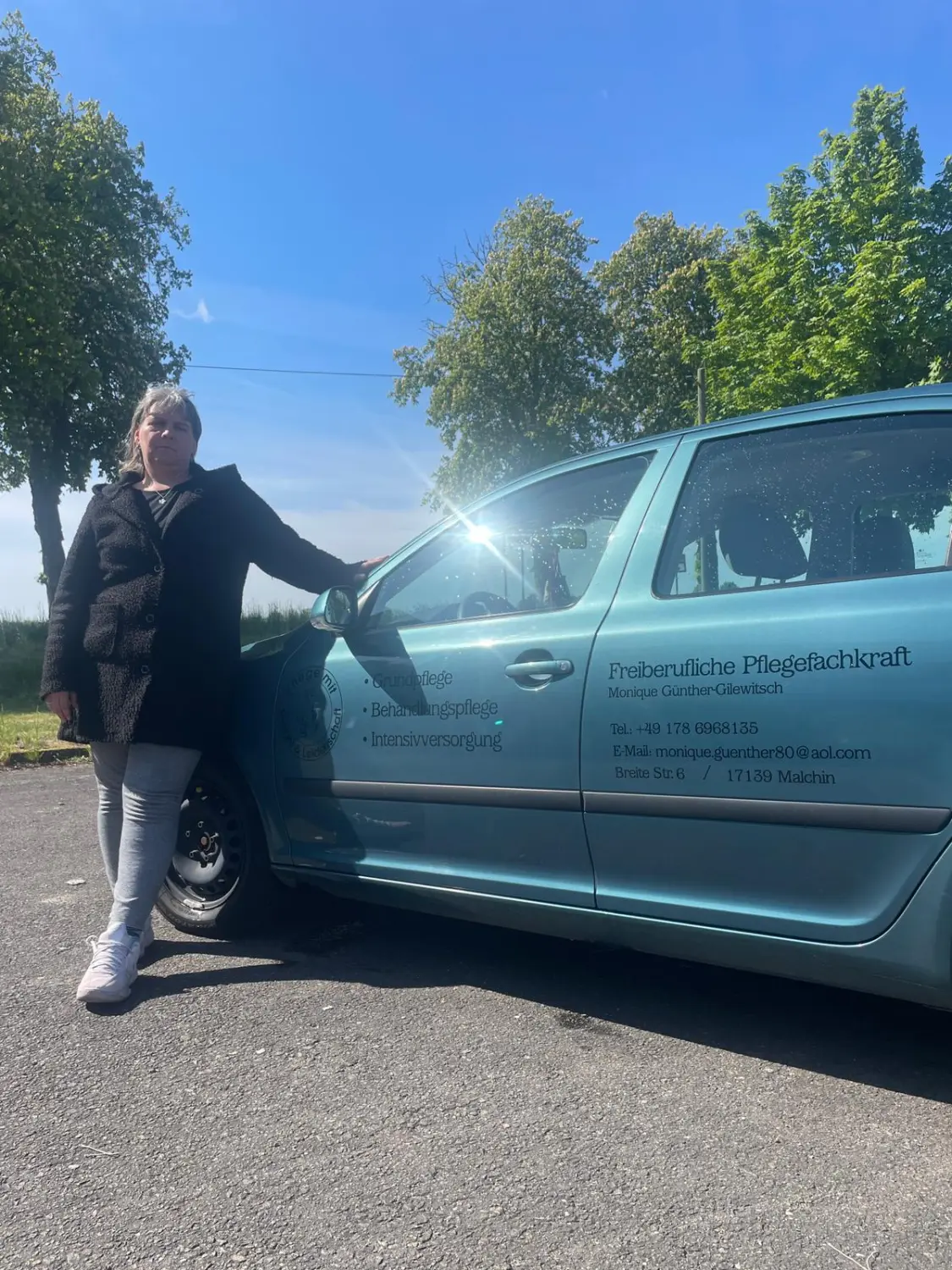 Pflegeengel Monique - Pflege mit Gefühl und Leidenschaft - Freiberufliche Krankenschwester steht neben einem Firmenwagen